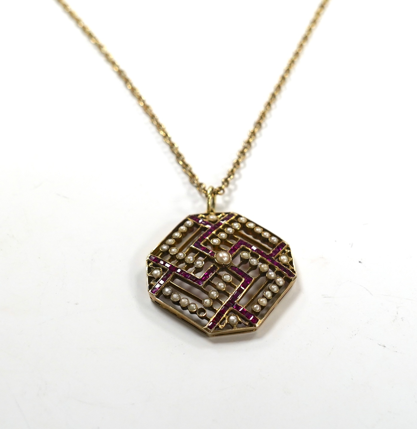 An Edwardian 15ct, ruby and seed pearl set octagonal pendant, 35mm, gross weight 9.7 grams, on a gilt metal chain.